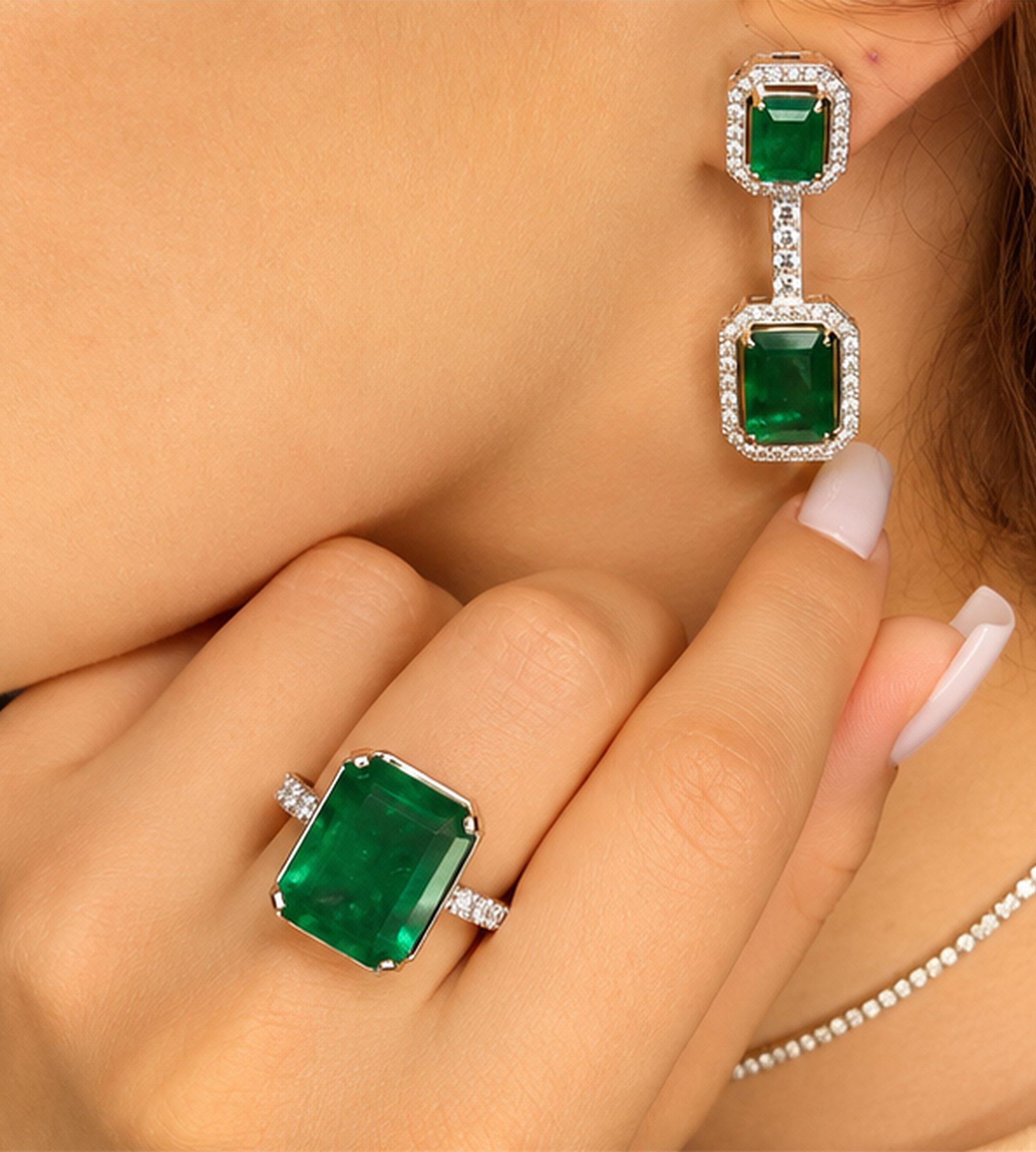 Emerald-cut emerald ring worn with matching emerald drop earrings and a diamond line necklace